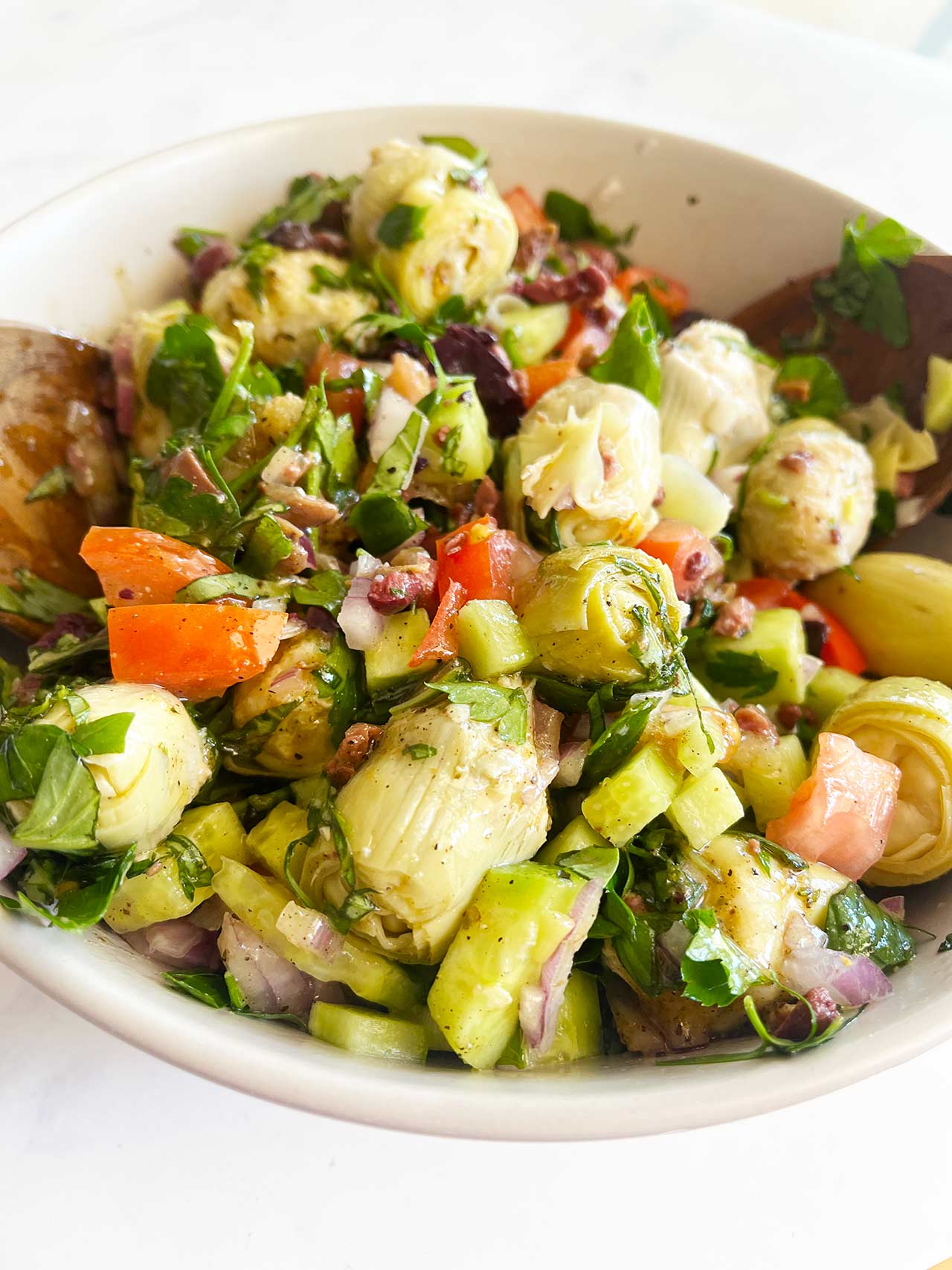 Dressing added to Artichoke Salad in a white mixing bowl and tossed.