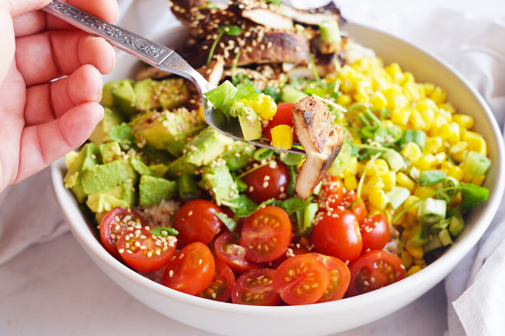 A hand holds a fork which holds a bit of this Chicken Poke Bowl.