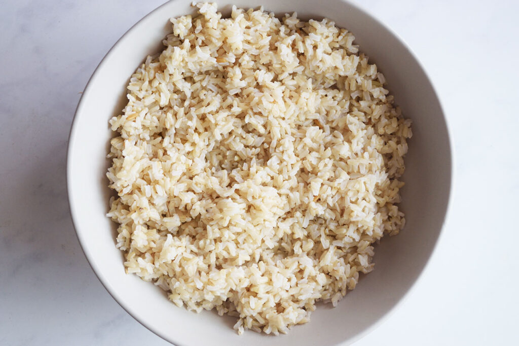 A bed of cooked brown rice covers the bottom layer of a bowl.