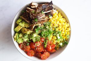Chicken Poke Bowl ingredients arranged over brown rice and garnished with fresh herbs and sesame seeds.