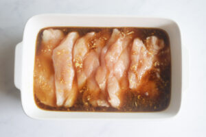 Marinade poured over chicken pieces in a white casserole dish.