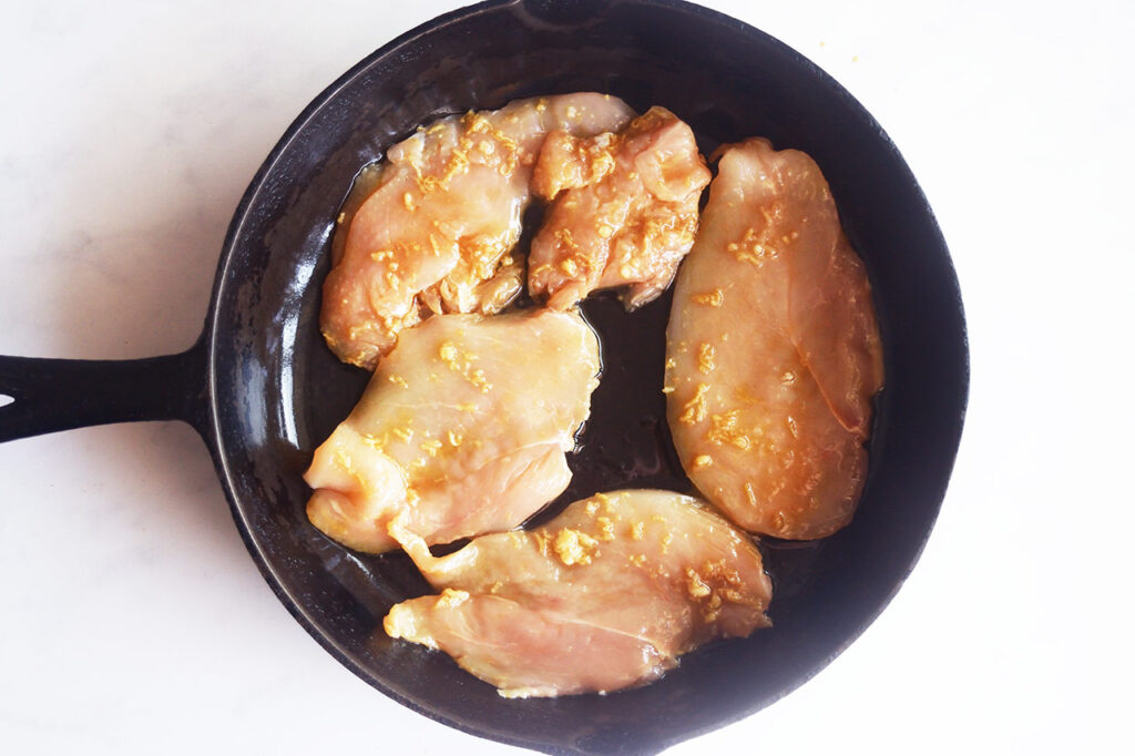 Marinated chicken in a skillet with a bit of marinade for cooking in.