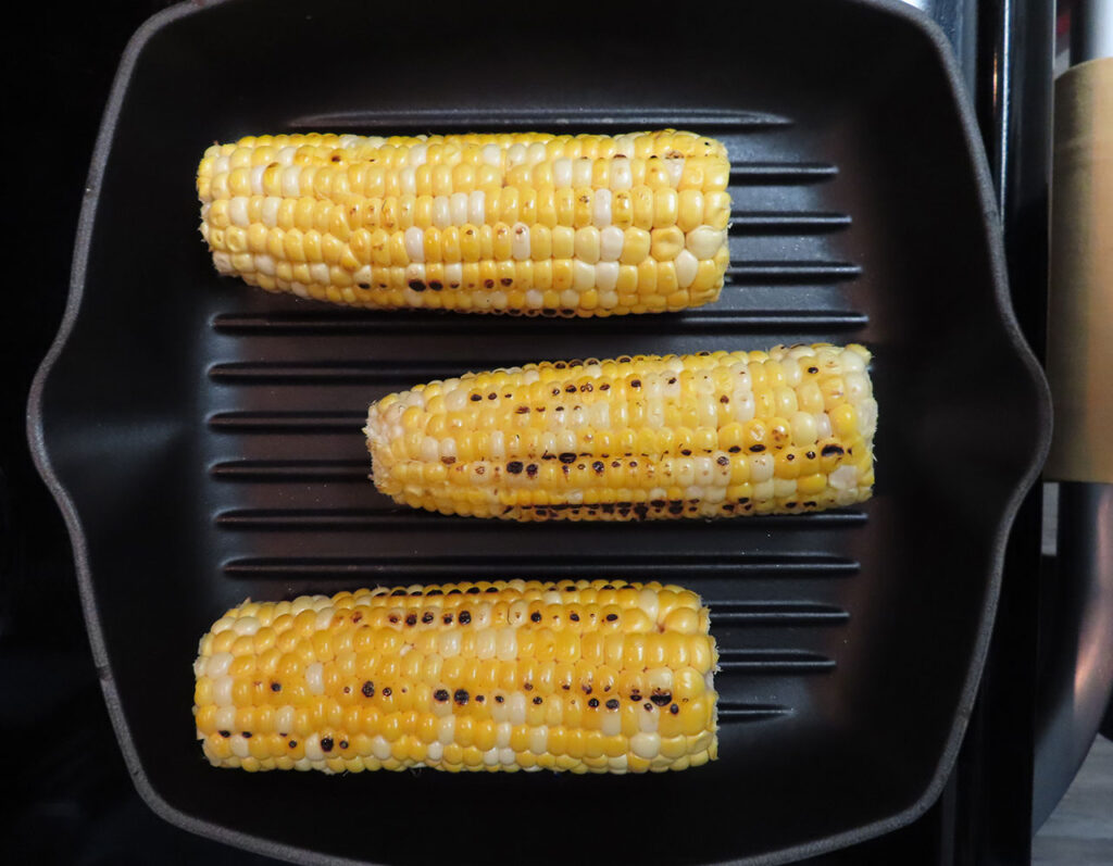 Partially grilled corn cobs on a grill pan.