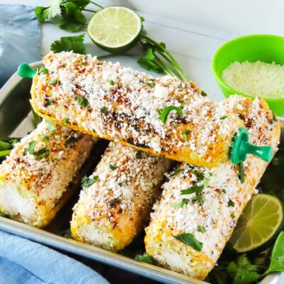 Front view of four corn cobs in a metal tray garnished with fresh cilantro.