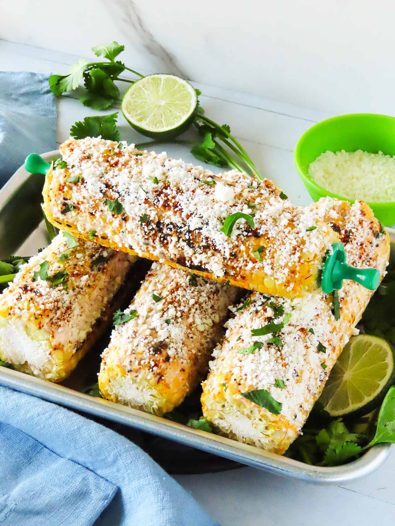 Front view of four corn cobs in a metal tray garnished with fresh cilantro.