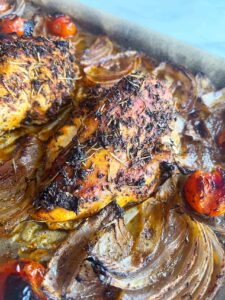 Close up of a chicken breast on a sheet pan with roasted veggies.