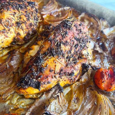 Close up of a chicken breast on a sheet pan with roasted veggies.