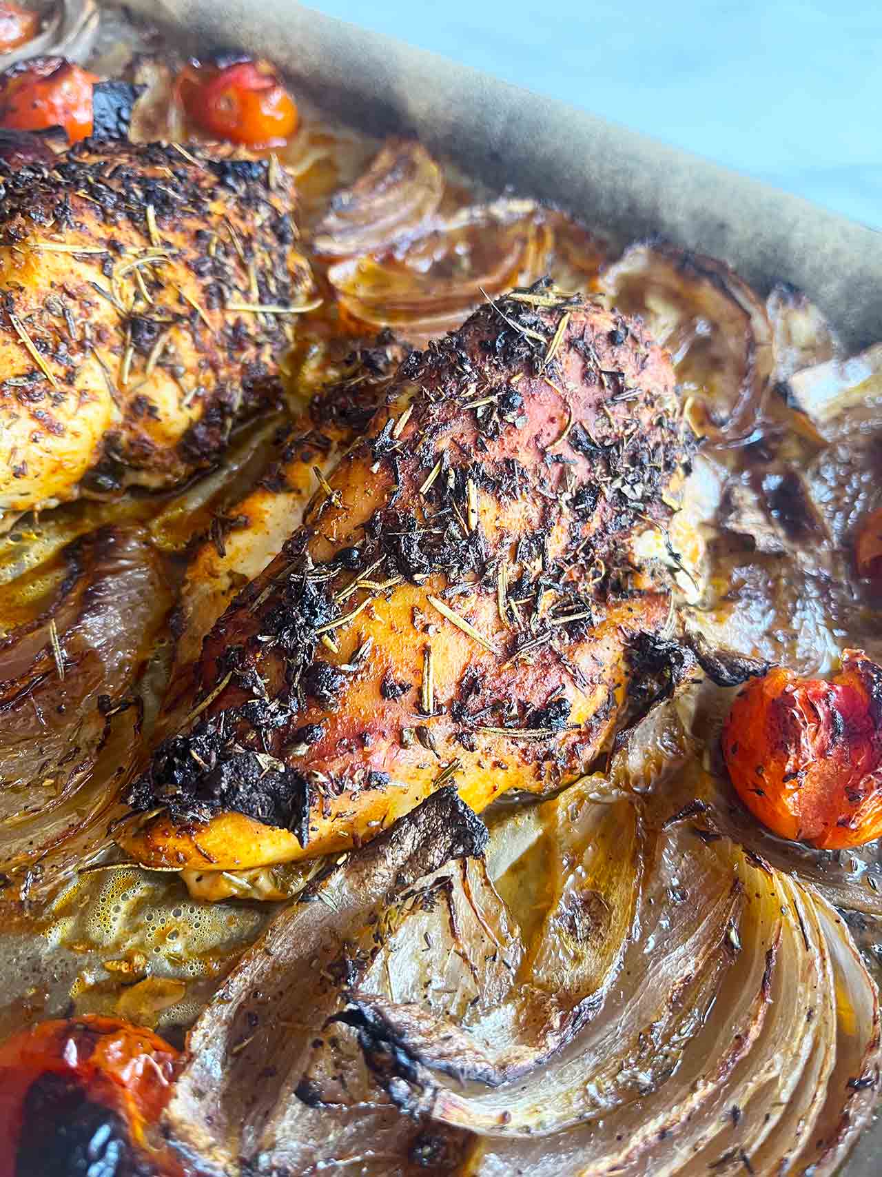 Close up of a chicken breast on a sheet pan with roasted veggies.