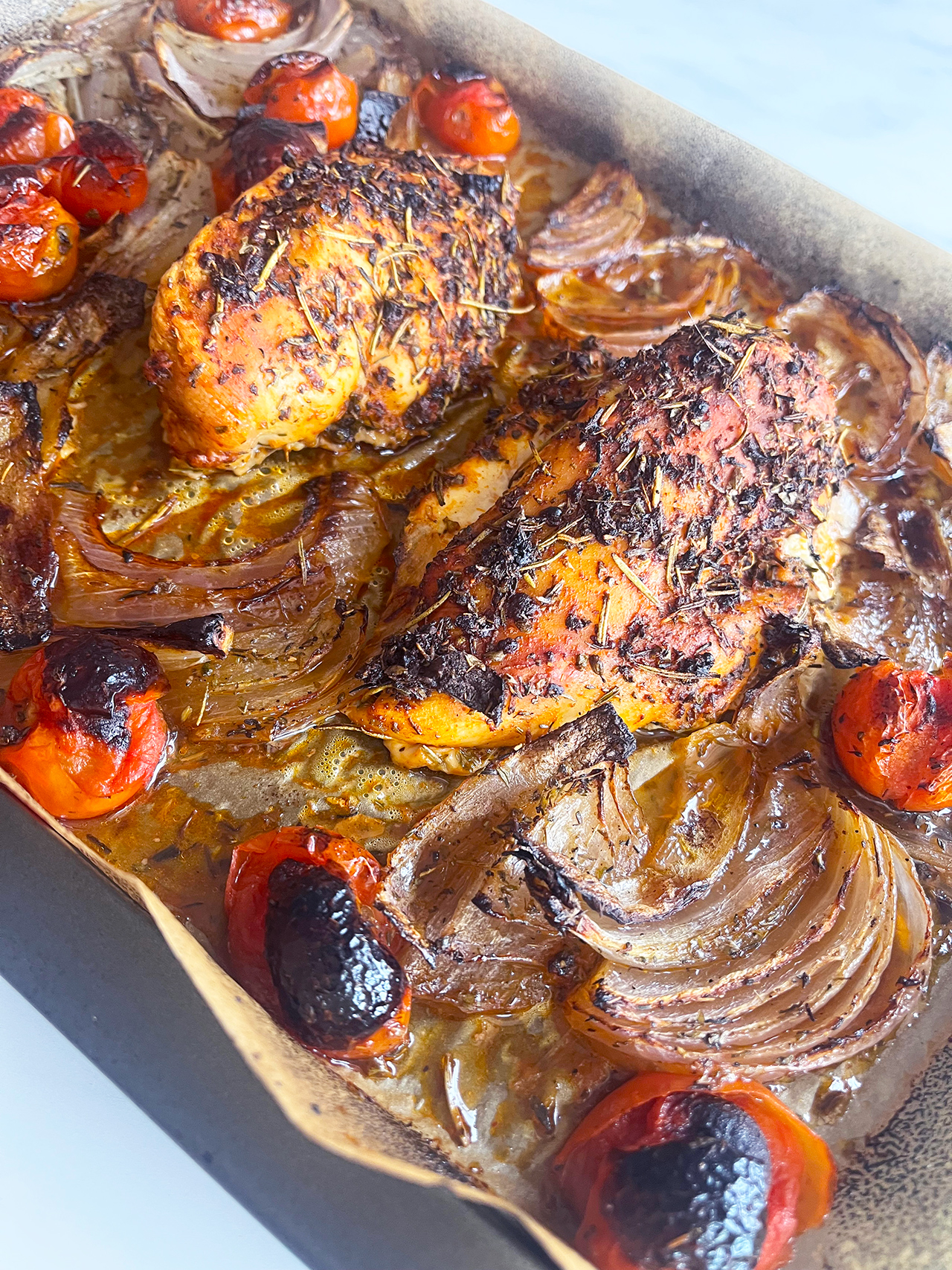 Side view of a sheet pan with cooked Mediterranean Sheet Pan Chicken.