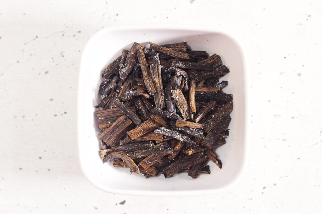 Small pieces of dried vanilla bean in a white bowl. Overhead focus.