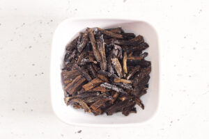 Small pieces of dried vanilla bean in a white bowl. Overhead focus.
