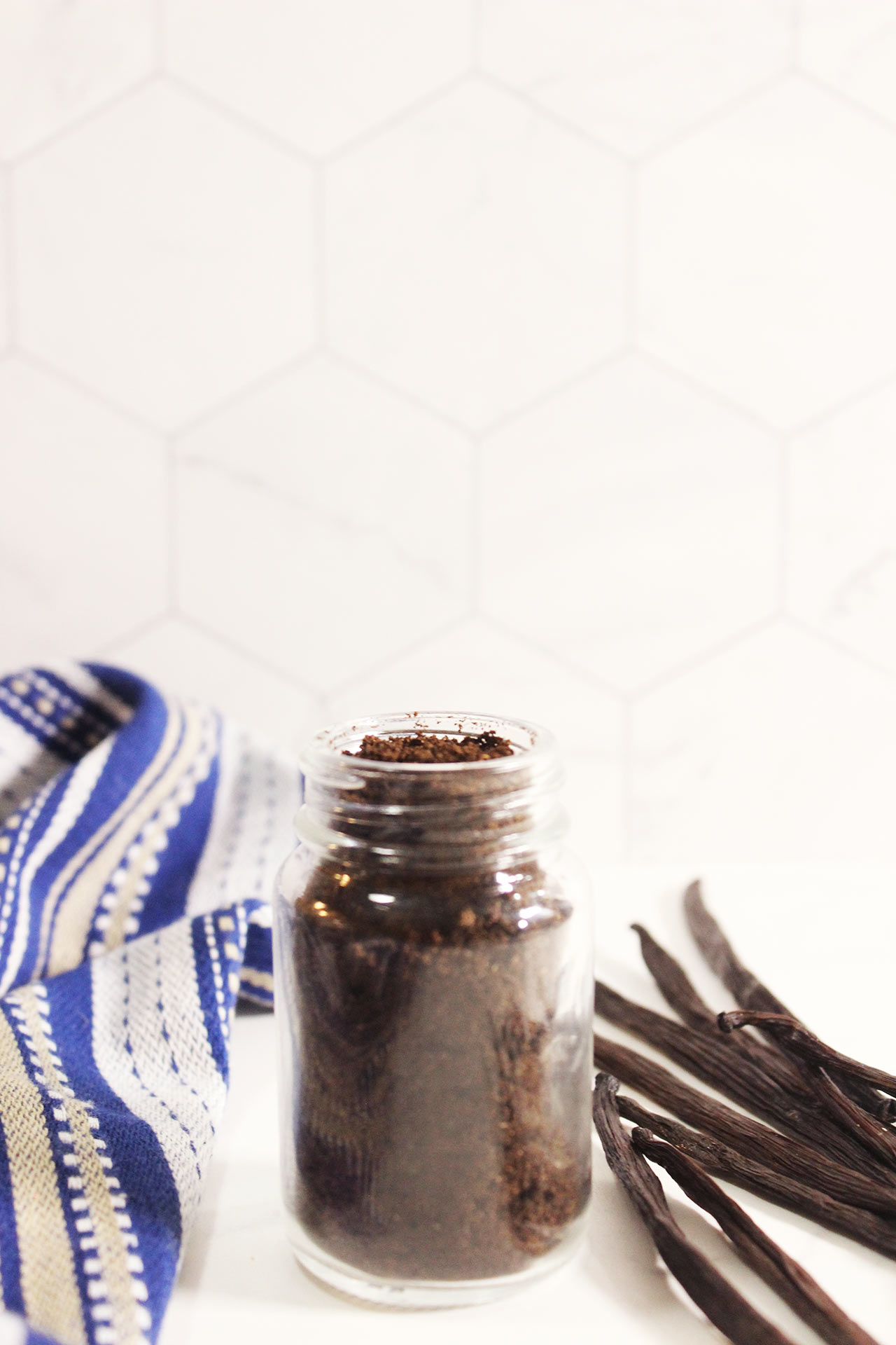Front view of a glass spice jar filled with vanilla powder. White background.