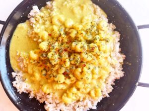 Overhead focus. A black pan filled with brown rice and topped with Coconut Curry Shrimp.