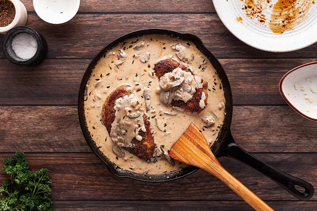 Chicken added to a skillet filled with sauce for Creamy Mushroom Chicken.