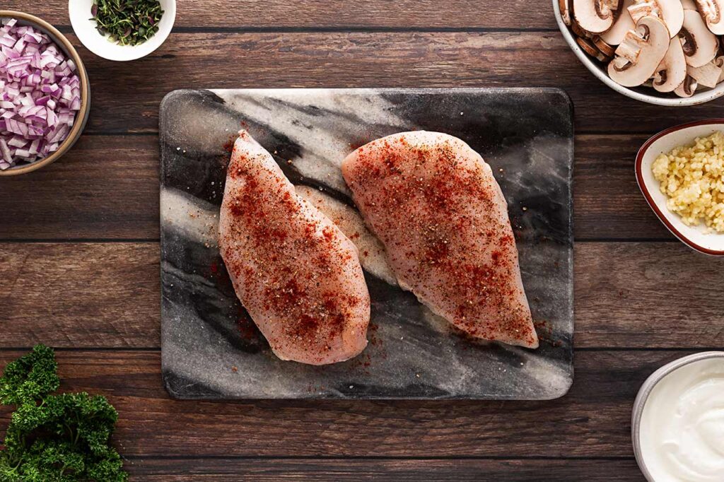 Two raw chicken breasts seasoned with spices. Overhead focus.