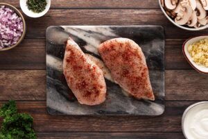 Two raw chicken breasts seasoned with spices. Overhead focus.