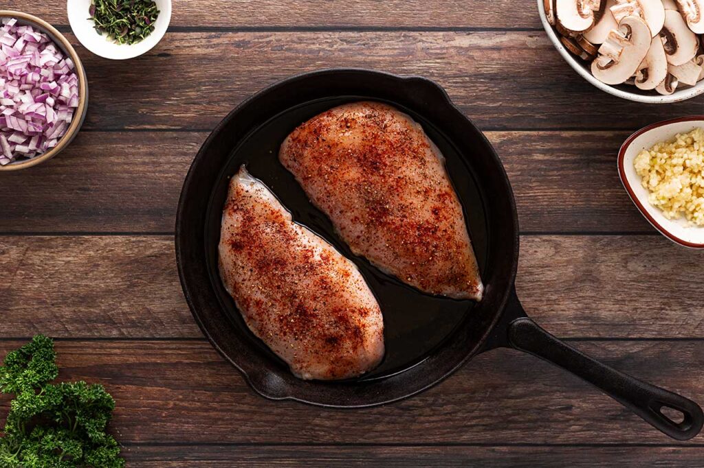 Seasoned chicken breasts in a cast iron skillet.