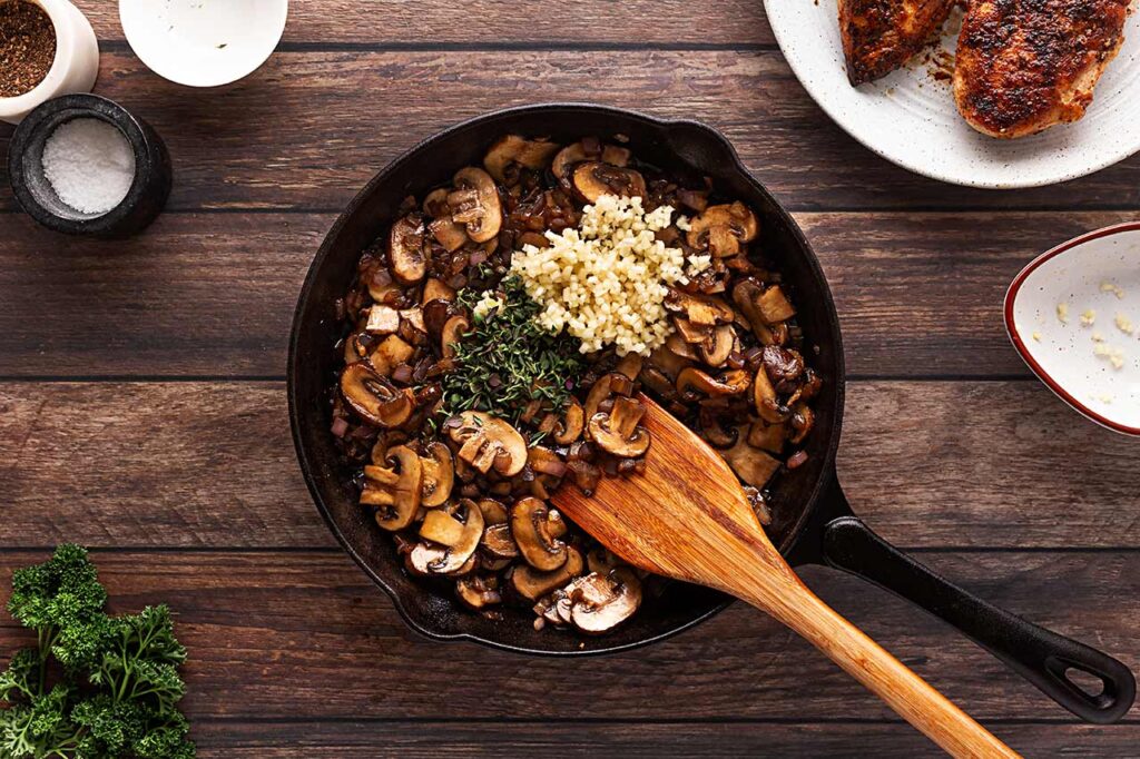 Herbs and garlic added to mushrooms and onions in a cast iron skillet.