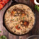 Overhead focus. A cast iron skillet filled with Creamy Mushroom Chicken sitting on a wood surface.