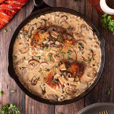 Overhead focus. A cast iron skillet filled with Creamy Mushroom Chicken sitting on a wood surface.