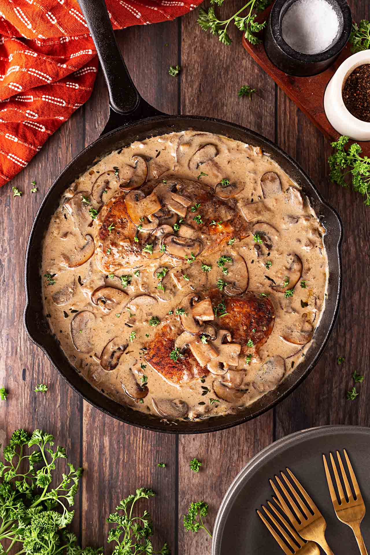 Overhead focus. A cast iron skillet filled with Creamy Mushroom Chicken sitting on a wood surface.