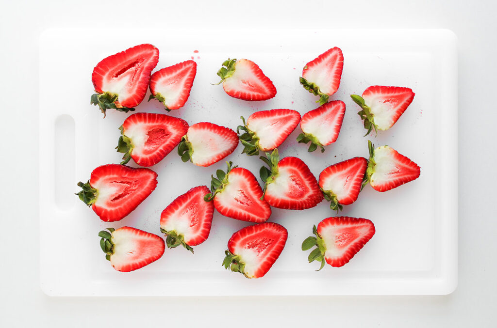Halved strawberries on a cutting board. Overhead focus.