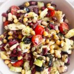 Overhead focus of a Mediterranean Dense Bean Salad in a white bowl on a white background.