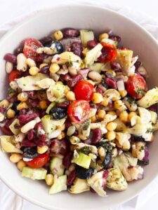 Overhead focus of a Mediterranean Dense Bean Salad in a white bowl on a white background.