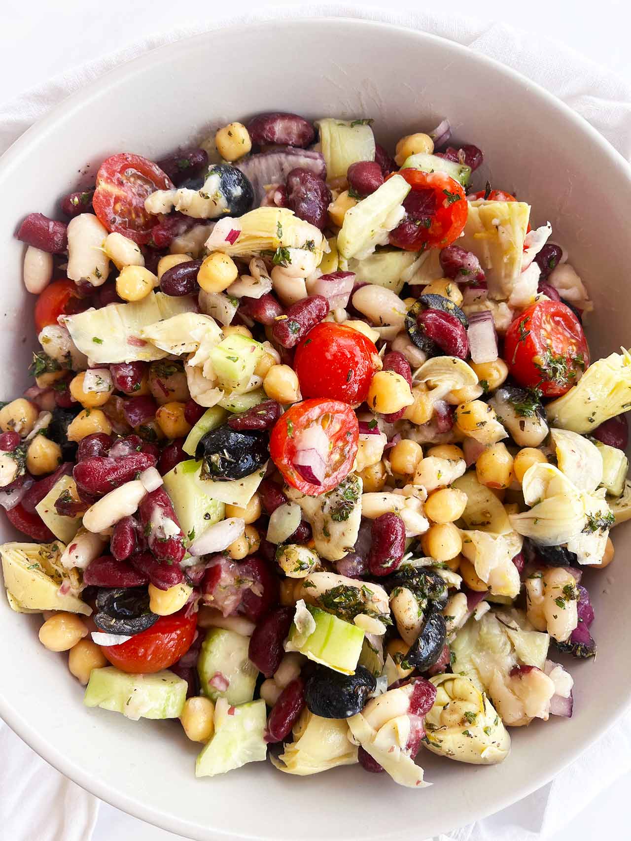 Overhead focus of a Mediterranean Dense Bean Salad in a white bowl on a white background.