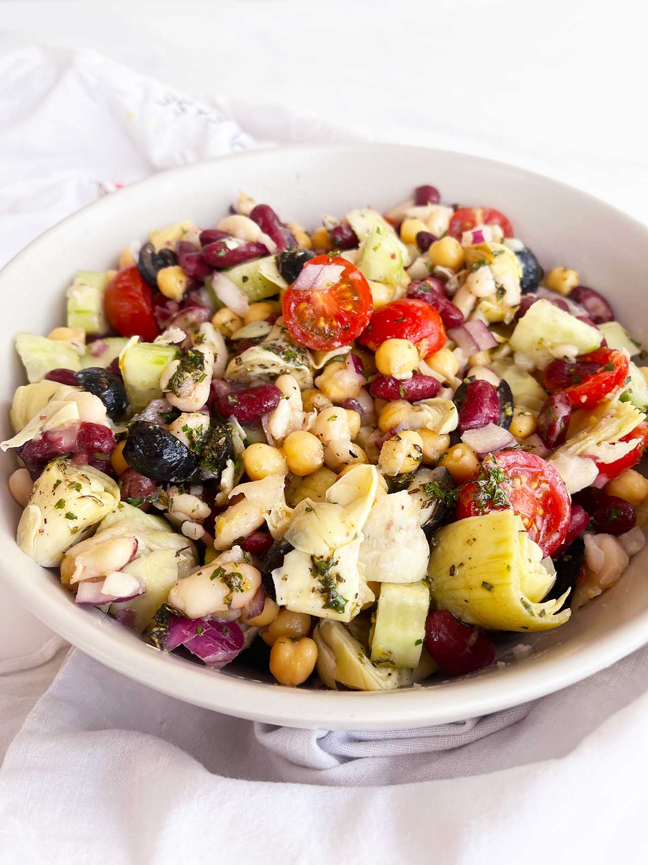Front view of a white bowl filled with Mediterranean Dense Bean Salad.