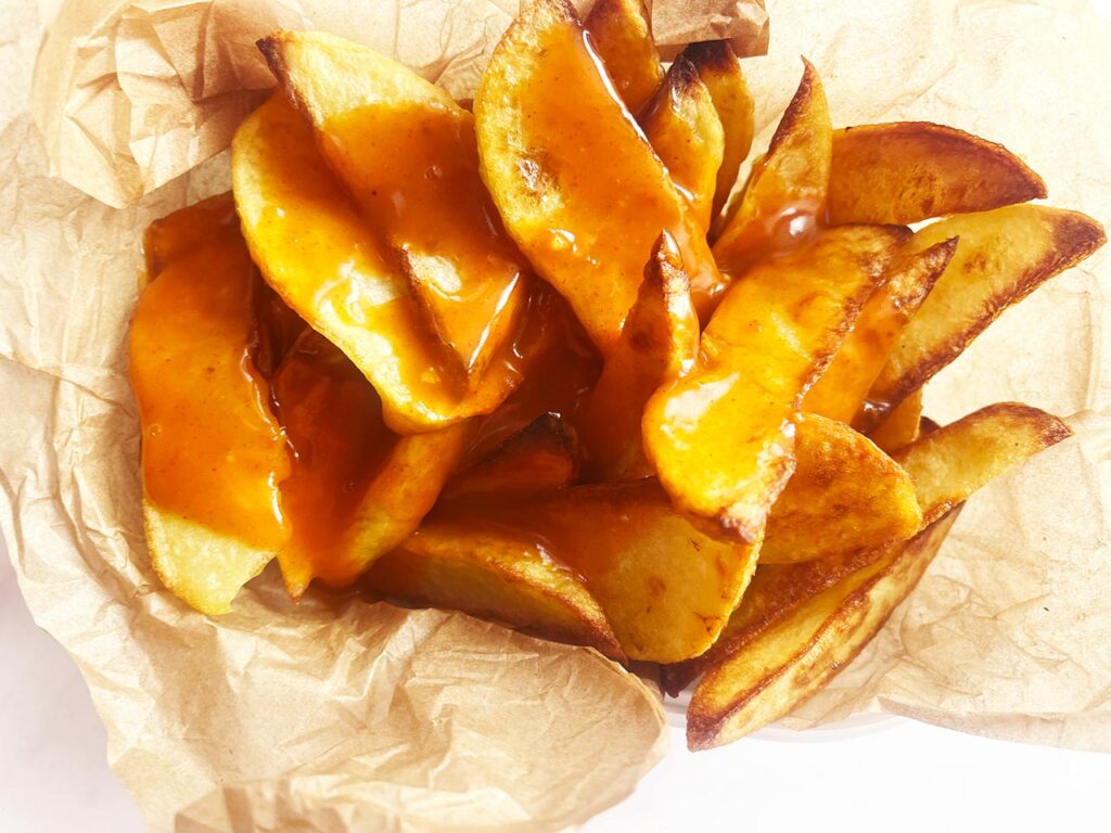 Bravas sauce poured over potato wedges in a parchment-lined basket.