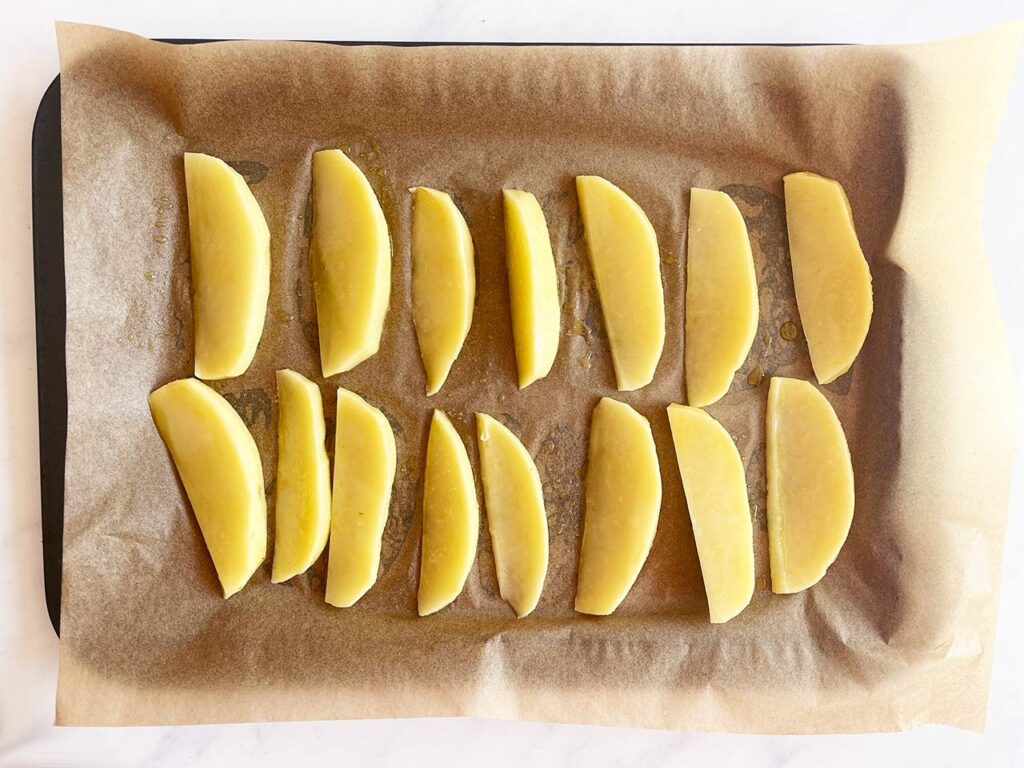 Raw potato wedges on a parchment-lined baking pan.