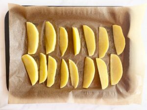 Raw potato wedges on a parchment-lined baking pan.