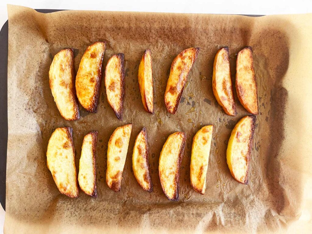 Baked potato wedges on a parchment-lined baking pan.