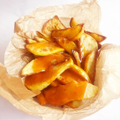 Patatas Bravas served in a parchment-lined basket. Front view.