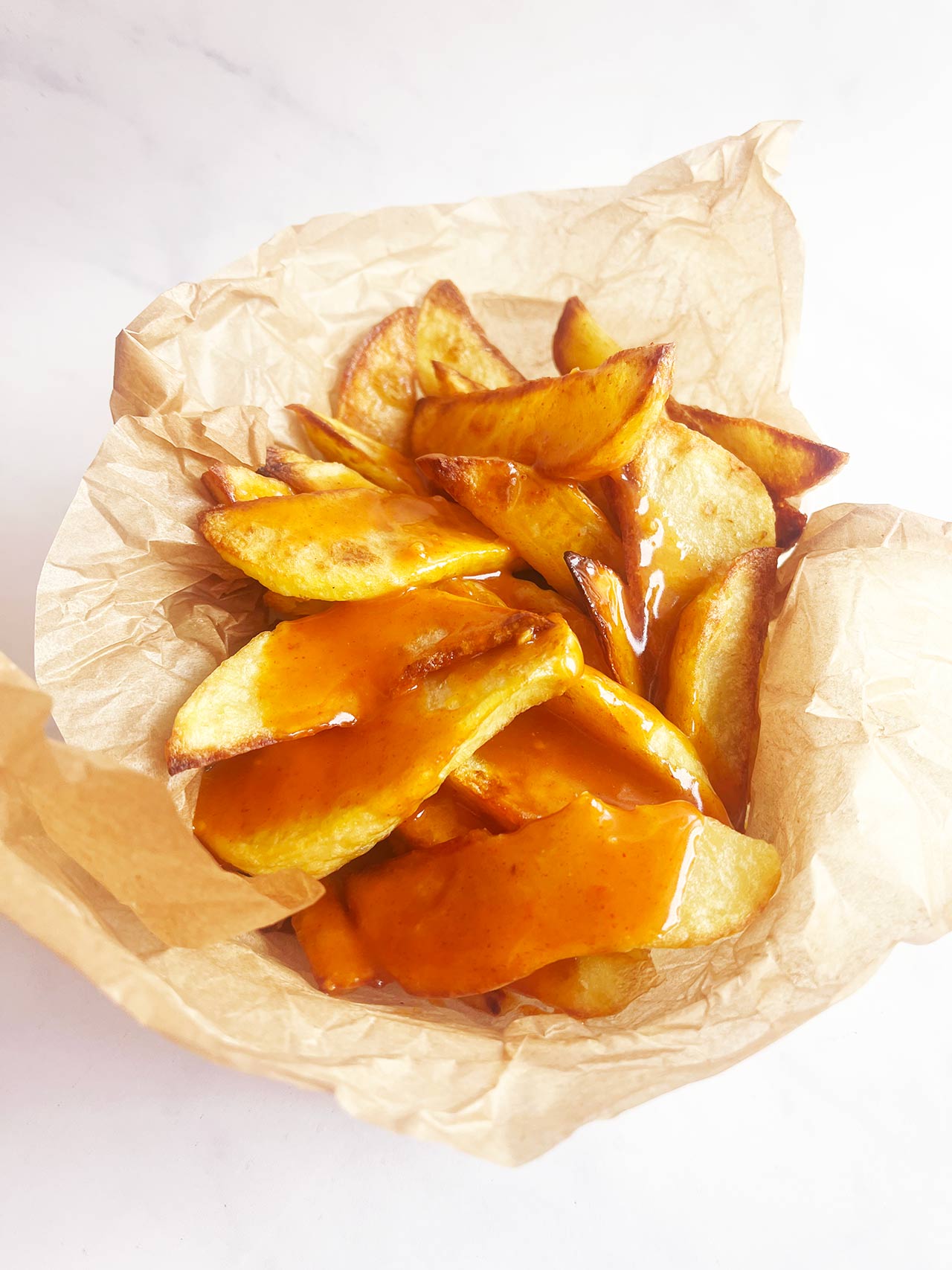 Patatas Bravas served in a parchment-lined basket. Front view.