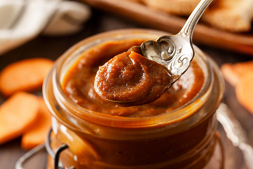 A spoon lifts a bit of Sweet Potato Butter from an open jar.