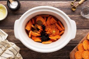 Sweet potato slices, spices, and molasses in a slow cooker crock.