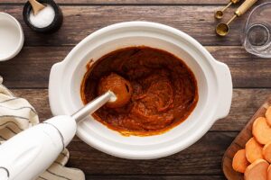 An immersion blender blending Sweet Potato Butter in a slow cooker crock.