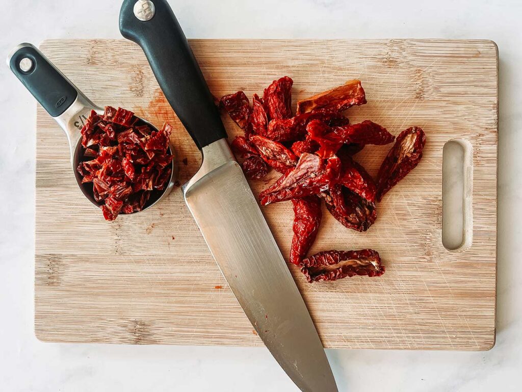 Chopped, sun-dried tomatoes on a cutting board with a knife.