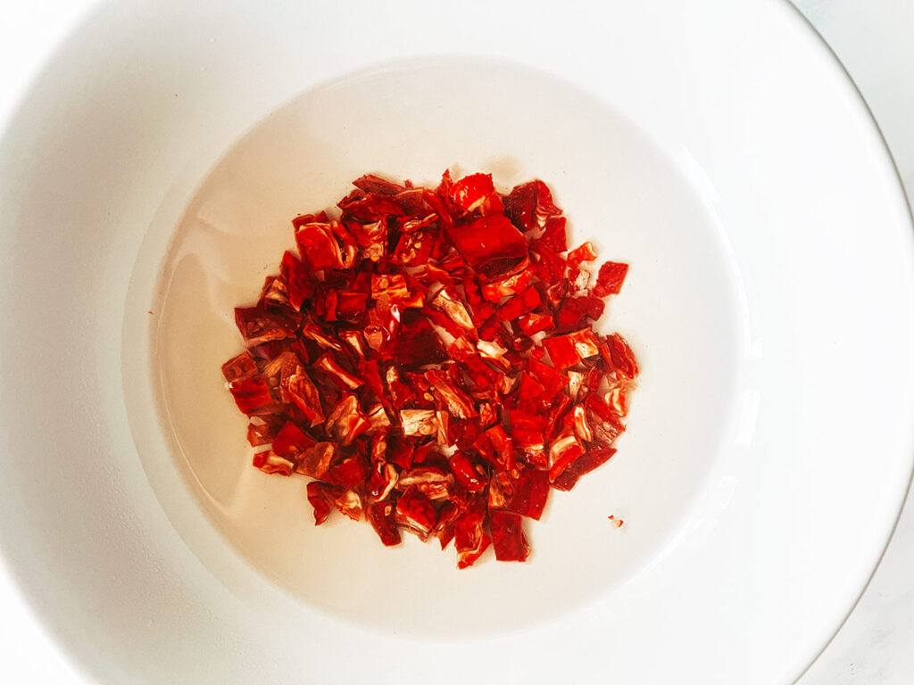Soaking dry-packed, sun-dried tomatoes in a bowl of hot water.