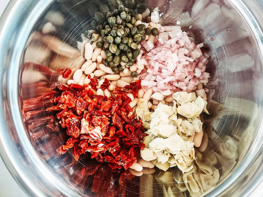 Ingredients for a Tuscan White Bean Salad added to a mixing bowl.