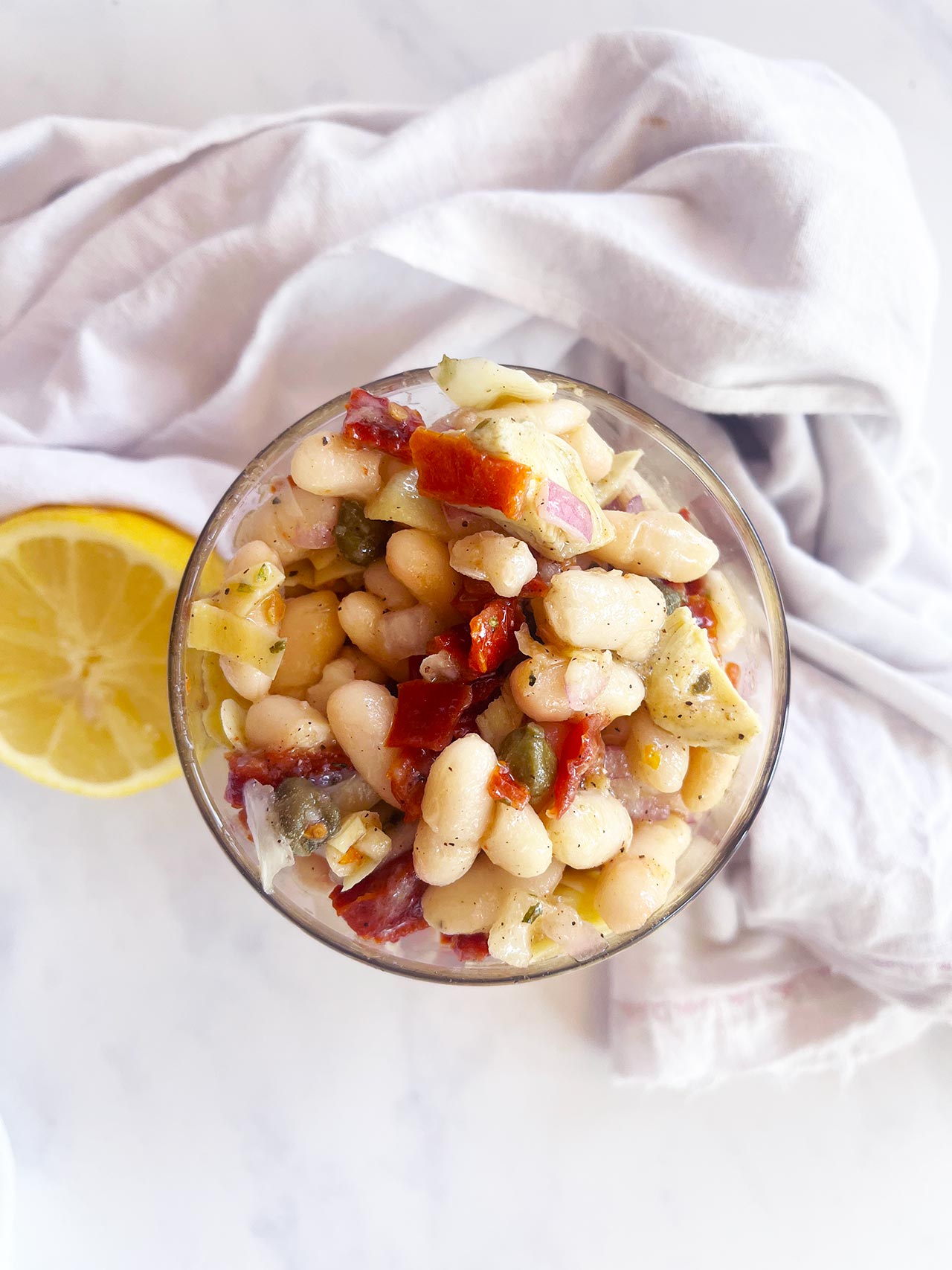 Overhead view. Open glass jar filled with Tuscan White Bean Salad. White background.