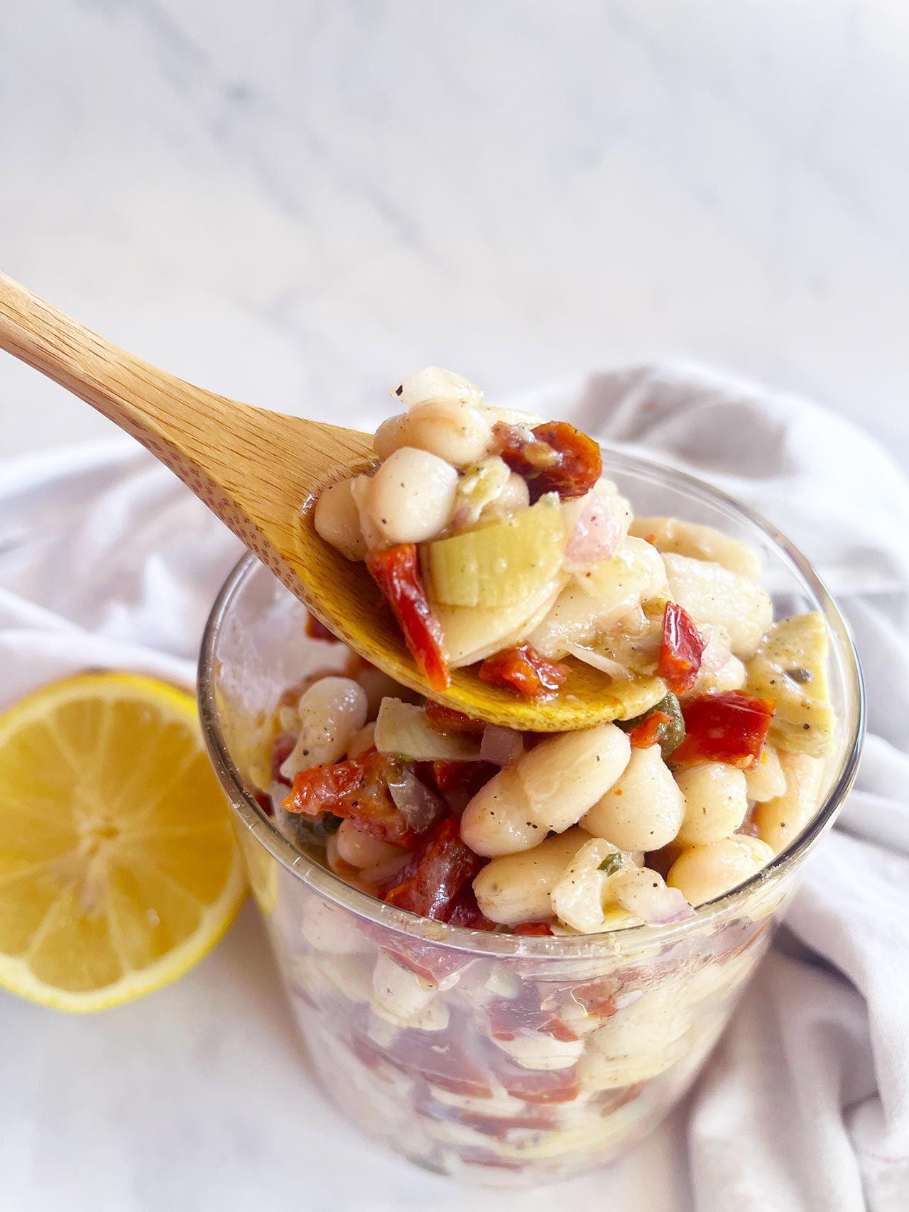 A wood spoon holds a spoonful of Tuscan White Bean Salad over an open jar.