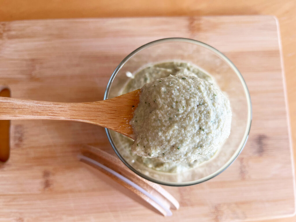 Overhead focus. A wood spoon lifts a spoonful of Artichoke Pesto out of an open jar.