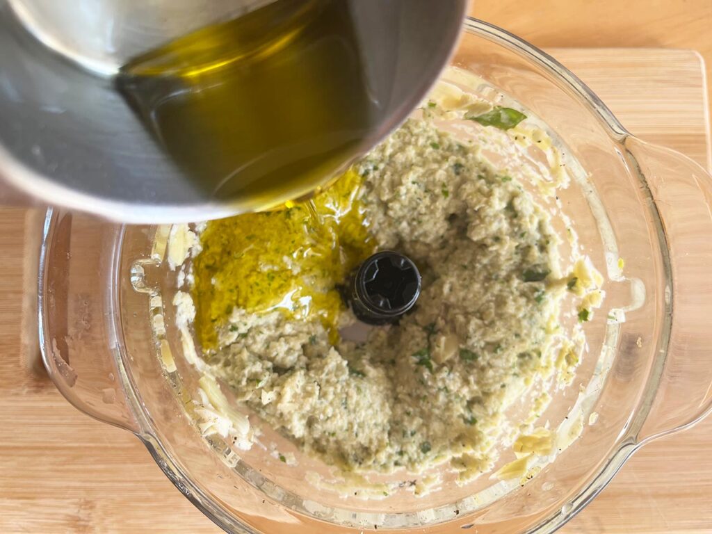 Adding oil to Artichoke Pesto in a food processor. Overhead focus.