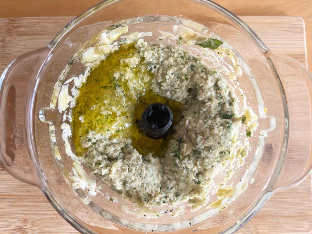 Oil added to Artichoke Pesto in a food processor. Overhead focus.
