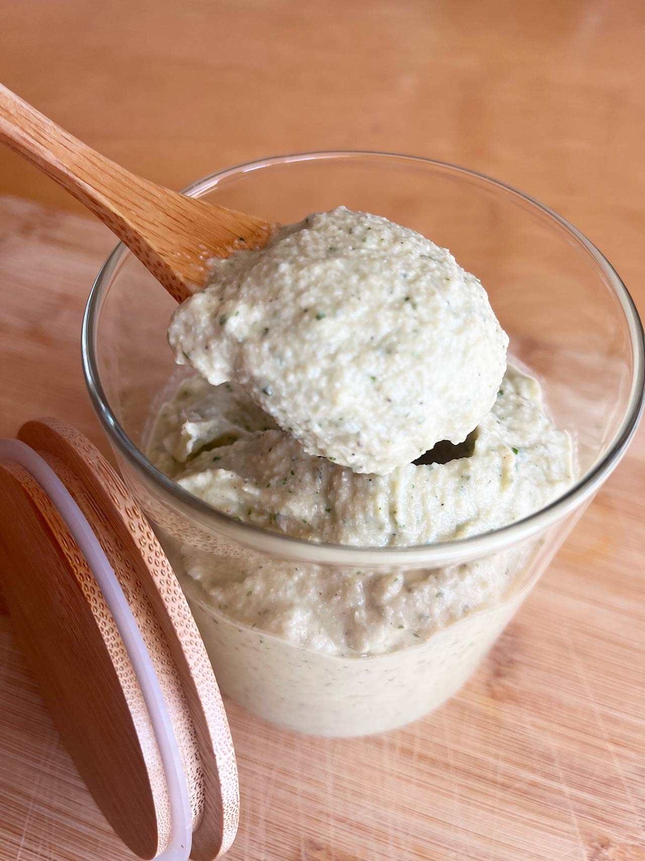 A wood spoon lifts some Artichoke Pesto our of a jar.