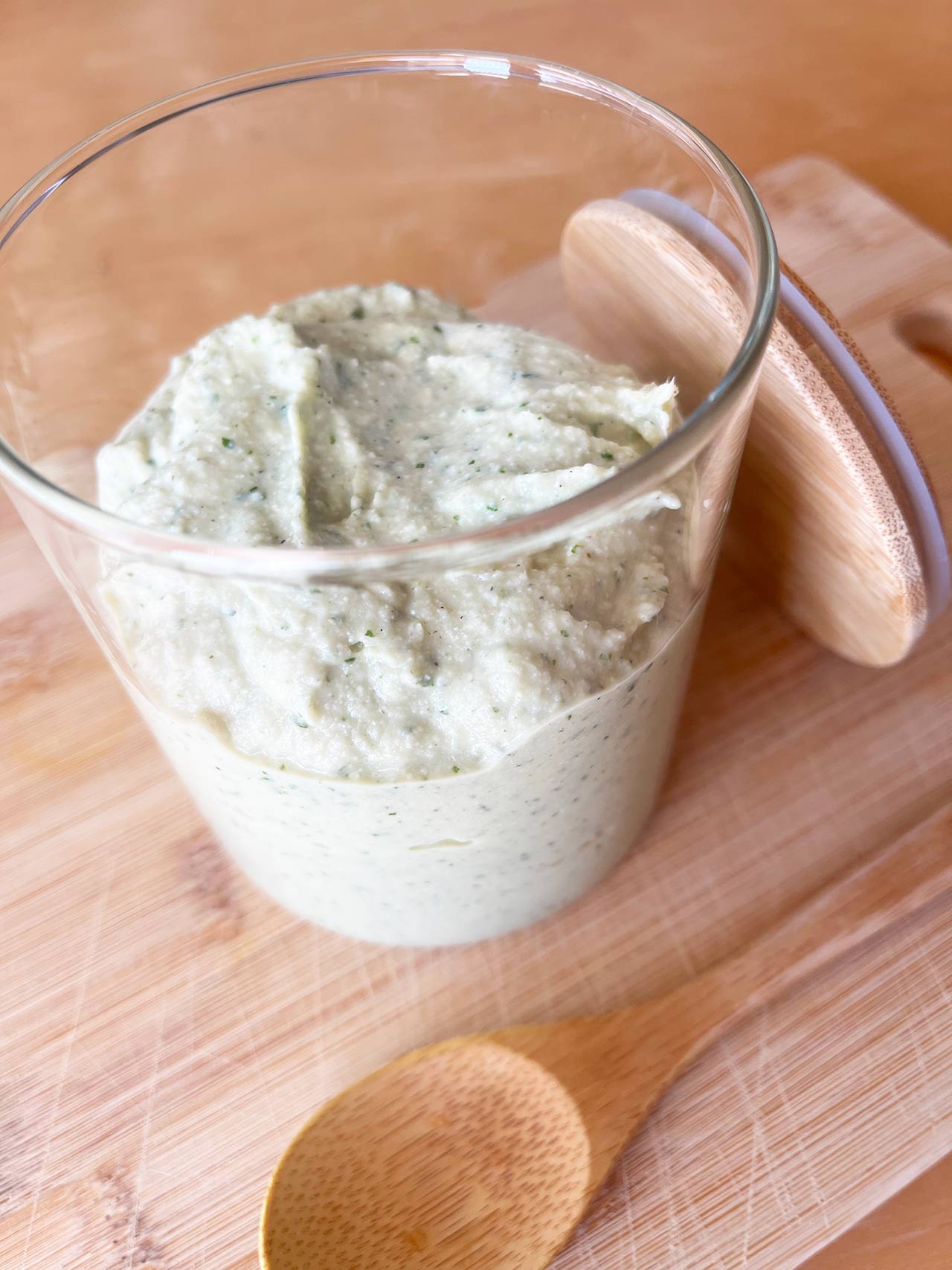 An open jar of Artichoke Pesto on a wood surface.