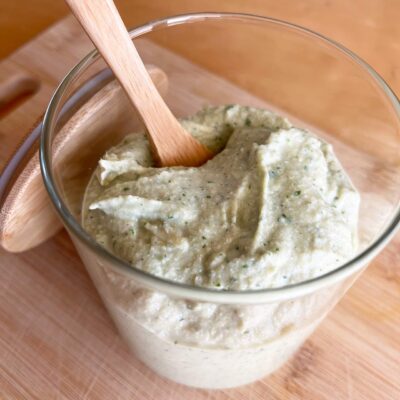 Partial overhead view of an open, glass jar of Artichoke Pesto with a wooden spoon resting in it.